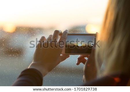 Female taking a photo of the sunset with a mobile phone through the window. 