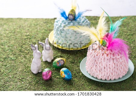 Mona de pascua, a pink and blue cakes eaten in Spain on Easter Monday, decorated with a chocolate egg and feathers of different colors. Easter decoration, selective focus. Space for text.