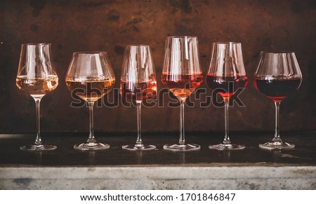 Various shades of Rose wine in stemmed glasses placed in line from light to dark colour on concrete table, rusty brown background behind. Wine bar, wine shop, wine tasting concept