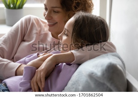Smiling mom embracing teen daughter resting together at cozy home. Happy family young adult parent mother and cute teenage school girl bonding, talking, enjoying sweet moment relaxing lying in bed.