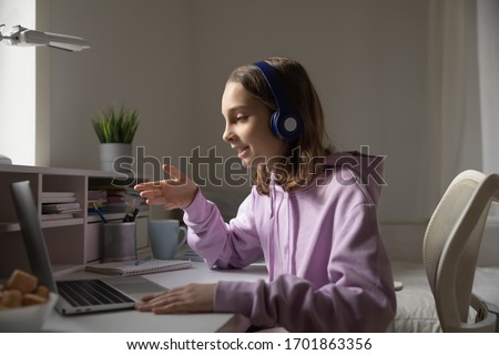 Teen girl school pupil wears headphones conference calling studying online with remote tutor from home. Teenage student using laptop talking in webcam video chat learning lesson with distance teacher. Royalty-Free Stock Photo #1701863356