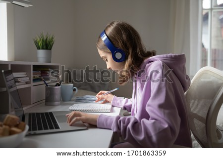 Teen girl school pupil wearing headphones studying online from home making notes. Teenage student distance learning on laptop doing homework, watching listening video lesson. Remote education concept Royalty-Free Stock Photo #1701863359