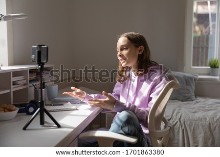Teen girl blogger influencer recording video blog concept speaking looking at smartphone on tripod at home table. Teenager social media vlogger shooting vlog, streaming online podcast on mobile phone. Royalty-Free Stock Photo #1701863380