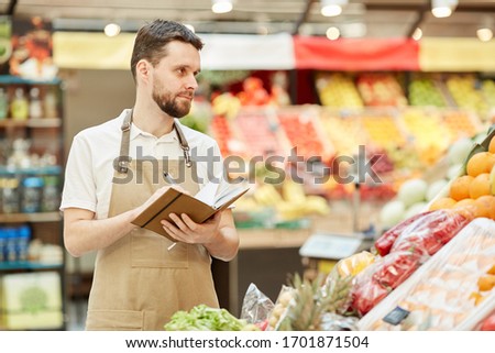 Waist up portrait of bearded farmer holding notebook while selling fresh fruits and vegetables at market stand, copy space