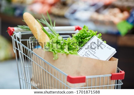 Background image of shopping cart with fresh groceries, focus on shopping list in paper bag, copy space