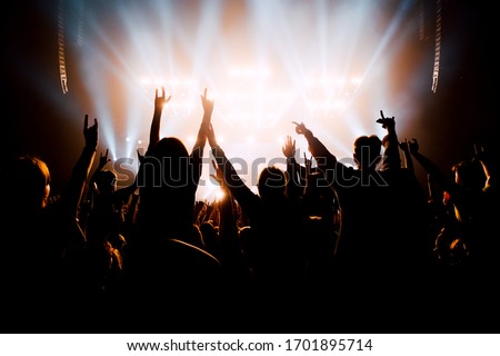 Crowd of people with raised up hands to the stage. Bright stage light silhouettes 