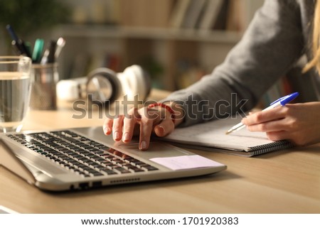 Close up of student girl hands comparing notes on laptop sitting on a desk at home at night
