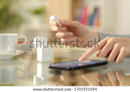 Close up of woman hands holding earbud checking smart phone on a desk at home