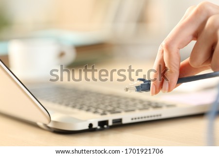 Close up of woman hands plugging ethernet cable on laptop on a desk