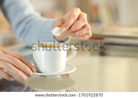 Close up of woman hand holding sugar cube over a coffee cup on a desk at home Royalty-Free Stock Photo #1701922870