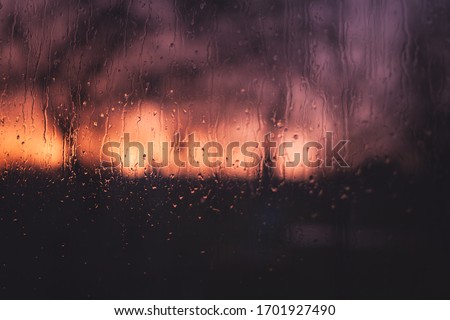 Raindrops on the window glass, Orange-violet tone, Rain during sunset, blurred background. Autumn pensive gloomy mood. Desktop background