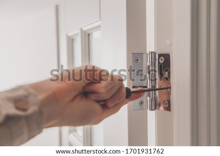 Man remove the door. Twists self-tapping screw with a screwdriver. Stainless door hinges on a white door Royalty-Free Stock Photo #1701931762