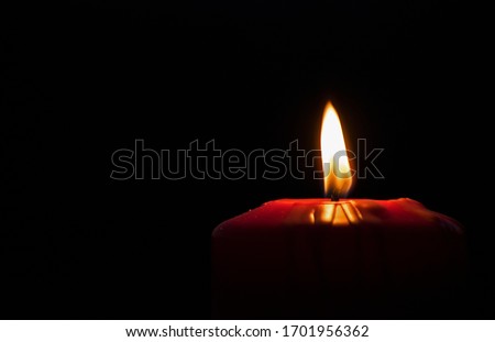 A lighted candle in someone's memory. Beautiful red holiday candle, on a black background. Christmas, Easter. Copy space. Royalty-Free Stock Photo #1701956362