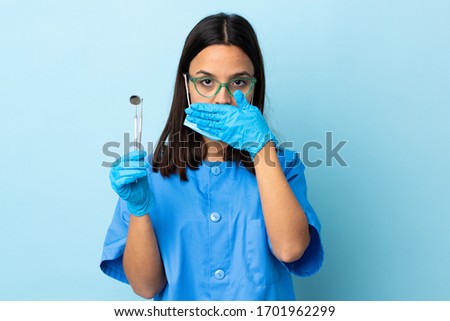Young brunette mixed race dentist woman holding tools over isolated background showing a sign of silence gesture