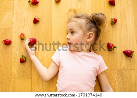 biracial playful cute beautiful little girl preschooler laying down floor playing and eating fresh organic newly harvested strawberries from local farmer's market. Promotes healthy eating. Lifestyle