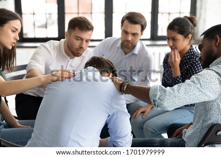 Multiethnic young people sit in circle participate in group psychological therapy together, diverse patients hug support comfort upset man patient at team counseling session, depression concept Royalty-Free Stock Photo #1701979999