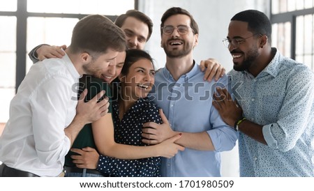 Overjoyed multiracial colleagues have fun laugh celebrate shared win or victory at workplace, happy diverse multiethnic coworkers hug show unity and support at work, teamwork, cooperation concept Royalty-Free Stock Photo #1701980509