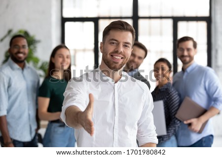 Smiling young Caucasian businessman stretch hand greeting meeting with new office employee or worker, happy male team leader or employer welcome newcomer or intern at workplace, recruitment concept Royalty-Free Stock Photo #1701980842
