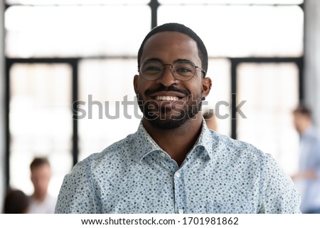 Headshot portrait of smiling African American male employee in glasses look at camera posing at workplace, happy motivated biracial man worker show confidence and leadership, employment concept