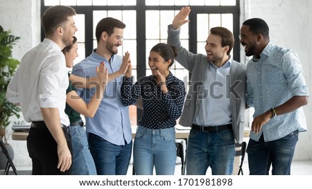 Overjoyed multiracial colleagues have fun celebrate shared business victory or win at workplace, happy diverse multiethnic businesspeople engaged in funny teambuilding activity in office together Royalty-Free Stock Photo #1701981898