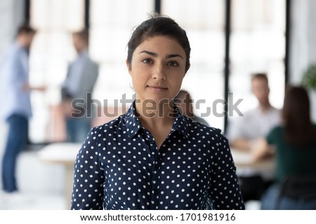 Headshot portrait of happy successful young Indian female employee posing in modern office, smiling confident millennial biracial woman worker show motivation at workplace, leadership concept
