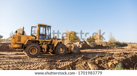 large yellow wheel loader aligns a piece of land for a new building. Preparation of the land for the auction. Leveling the landscape and adding sand for construction. Banner wallpaper. Royalty-Free Stock Photo #1701983779