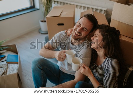 Top view photo of young happy couple drinking coffee while cardboard boxes are all around them. Young couple is moving in to their new home.