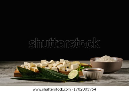 Fresh tofu pieces on bamboo leaves, on a wooden board near soy sauce, rice, ginger and lime.On a black background.Space for text.