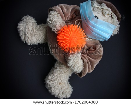 a toy bear lies on a dark gray background in a medical mask on his face and holds the symbol of coronovirus covid 19 in its paws