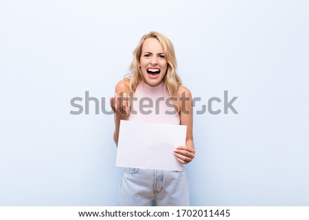 young blonde woman looking desperate and frustrated, stressed, unhappy and annoyed, shouting and screaming holding a sheet of paper