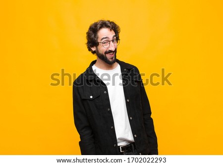 young crazy handsome man with a big, friendly, carefree smile, looking positive, relaxed and happy, chilling against orange wall