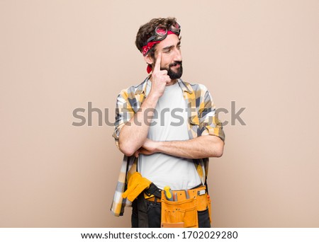 young housekeeper man with a concentrated look, wondering with a doubtful expression, looking up and to the side against flat wall