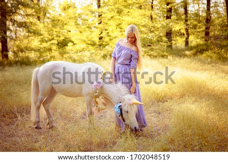 Blonde Woman in purple dress hugging white unicorn horse. Dreams come true. Fairy tale.