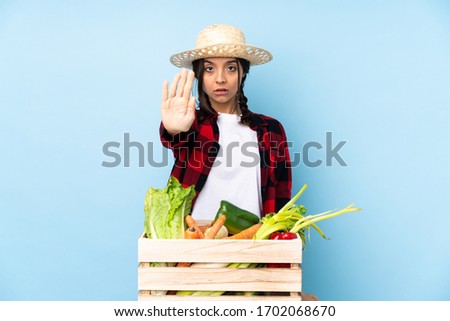 Young farmer Woman holding fresh vegetables in a wooden basket making stop gesture