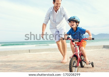 Father and son learning to ride a bicycle at the beach having fun together Royalty-Free Stock Photo #170208299