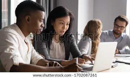 Concentrated diverse sit at desk brainstorm working on laptop together, focused multiracial coworkers talk discuss business ideas cooperate using computer at office briefing, collaboration concept Royalty-Free Stock Photo #1702087261