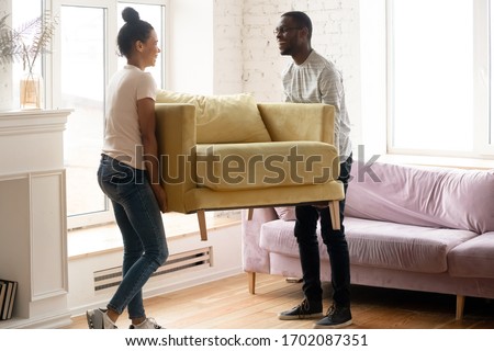 Young happy african american couple moving and carry table. Attractive family of diverse woman and man relocation furniture in new home. Husband and wife perform permutation. Royalty-Free Stock Photo #1702087351