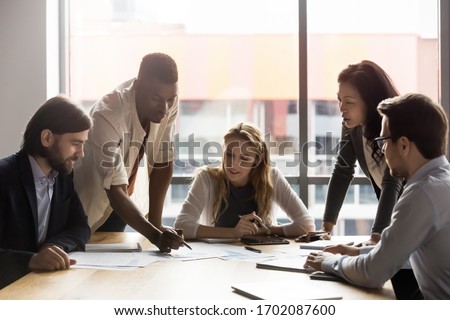 Focused multiracial businesspeople gather at desk brainstorm discuss company financial paperwork at meeting together, concentrated diverse colleagues talk negotiate at briefing in boardroom Royalty-Free Stock Photo #1702087600