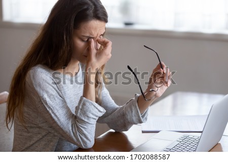 Head shot exhausted young woman taking off glasses, suffer from eyes strain due to computer overwork. Tired unhealthy millennial mixed race lady having painful feelings, blurred vision syndrome. Royalty-Free Stock Photo #1702088587