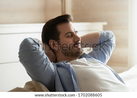 Peaceful young bearded man enjoying weekend lazy time alone at home, daydreaming on comfortable couch, head shot. Side view tranquil millennial man napping resting with closed eyes, sitting on sofa. Royalty-Free Stock Photo #1702088605