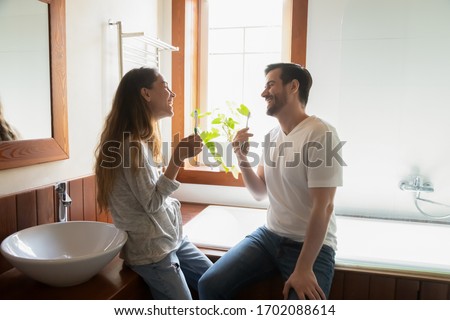 Happy young family couple chatting communicating while cleaning teeth together in bathroom. Excited millennial newlyweds laughing joking enjoying doing morning hygiene routine at home or hotel. Royalty-Free Stock Photo #1702088614