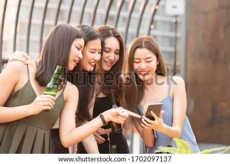 Group of young beautiful happy asian women holding bottle of beer chat together with friends while celebrating dance party on outdoor rooftop nightclub with copy space for advertising.