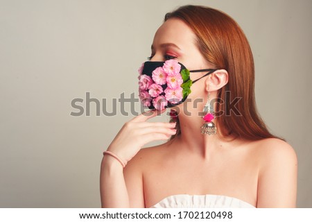 Girl with gorgeous long hair in an antiviral mask. Fashion photo on the cover of the magazine. Pandemic, virus, coronavirus, masked girl spring has come. Spring fashion, model in a mask of flowers