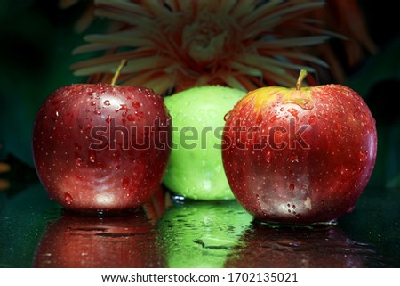 Apples: Red and green apples shot up close on a mirror and sprayed with water to cause reflections, against a dark background.
