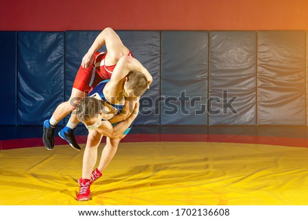 The concept of fair wrestling. Two greco-roman  wrestlers in sportwears makes throw through the back on a wrestling carpet in the gym.The concept of male wrestling and resistance