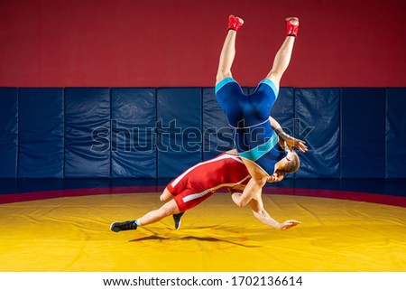 The concept of fair wrestling. Two greco-roman  wrestlers in sportwears makes throw through the back on a wrestling carpet in the gym.The concept of male wrestling and resistance