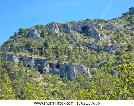 Photo of a landscape with a caves on a rocky and verdant provencal hill. This photo was taken very close of Fontaine de Vaucluse in Provence.
