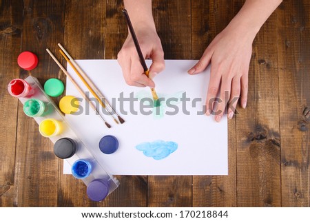 Hand holding brush with paints and paper on wooden background