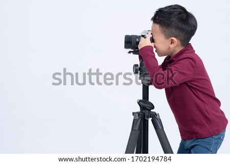 Portrait of little boy wearing red sweater standing taking photo with film camera isolated on grey background free from copy space.