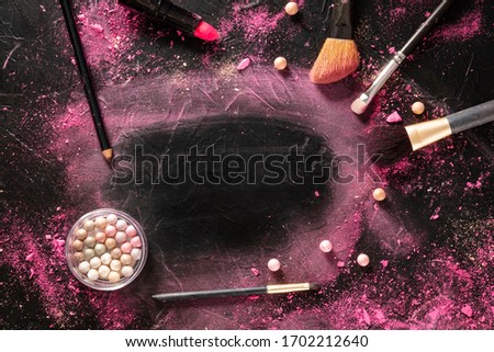 A make-up brush with crushed cosmetics, brushes, and lipstick on a black background, with a place for text, a beauty frame for a makeup school